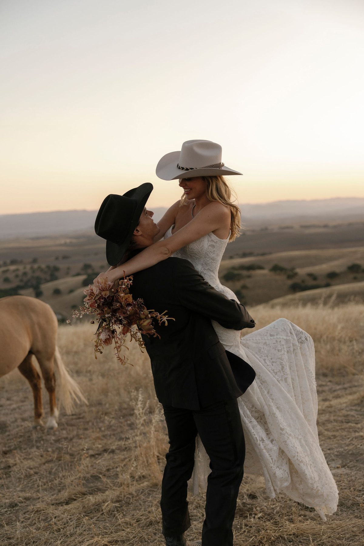 The couple embracing on the ridge at sunset, a palomino grazing nearby