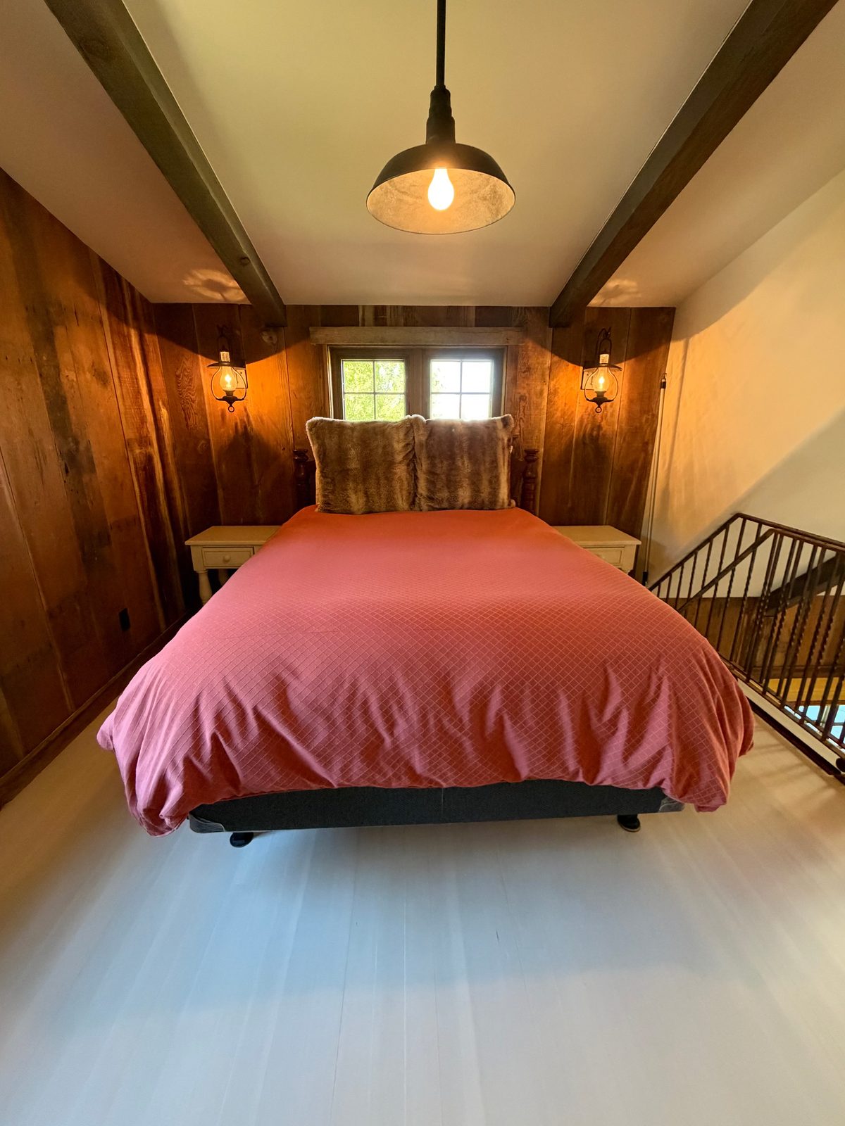 A guest room with a red quilt and wood-paneled walls